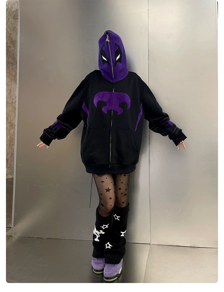A person wearing a Seakoff Dark Hero Hoodie, star-patterned sheer tights, and black leg warmers with white stars stands before a metallic wall, arms outstretched. Purple shoes add to the edgy streetwear vibe captured by this oversized black and purple superhero zip-up sweatshirt.