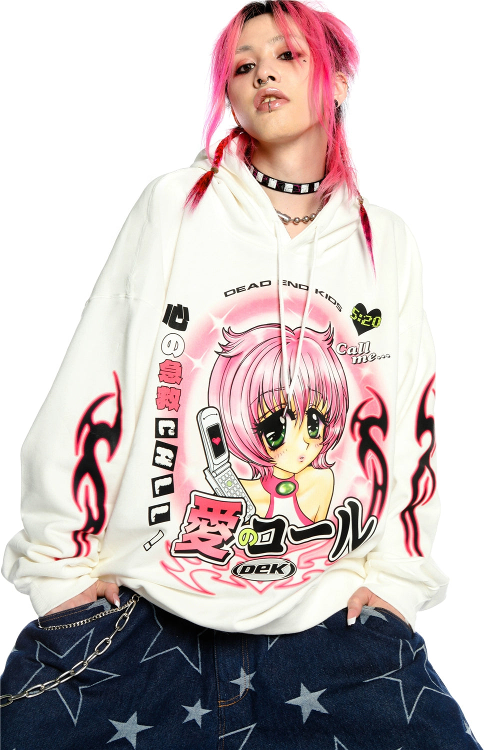 A person with pink hair confidently embraces the Y2K aesthetic in a Seakoff white hoodie, featuring a retro manga girl graphic. Paired with star-patterned wide-leg jeans and accessorized with a choker and chain, the plain backdrop highlights their bold, kawaii style.