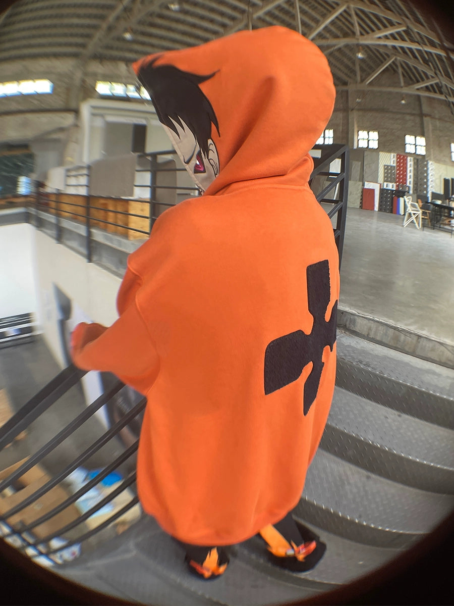 In a spacious industrial-style building, someone wearing the Seakoff Fire Force Inspired Orange Zip-Up Hoodie - 400GSM Oversized Anime Streetwear stands on an indoor staircase. The back displays a large black symbol, and the hood features a stylized character design.