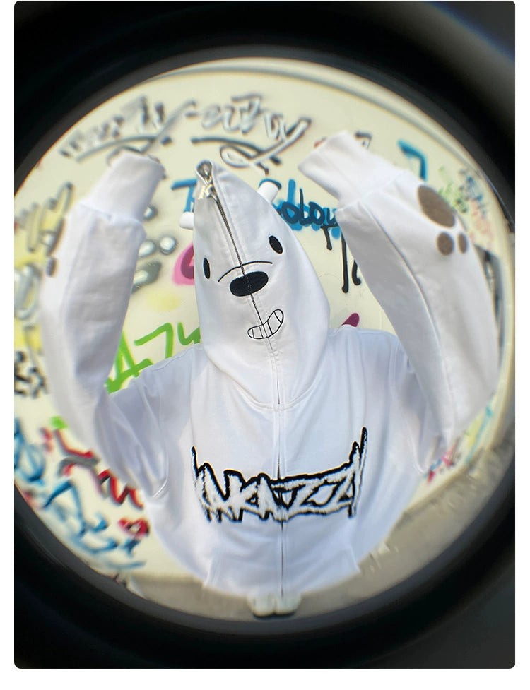 A person in a Seakoff Cute White Bear Hoodie with a polar bear design and black embroidery raises their arms. The hoodie boasts bear prints on the sleeves and a graphic logo on the front. A colorful graffiti background, captured through a fisheye lens, enhances the playful vibe.