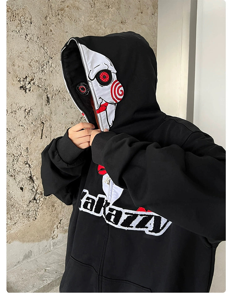 A person adjusts the hood of a Seakoff Saw-Inspired Hoodie, a black oversized zip-up sweatshirt featuring Billy the Puppet&