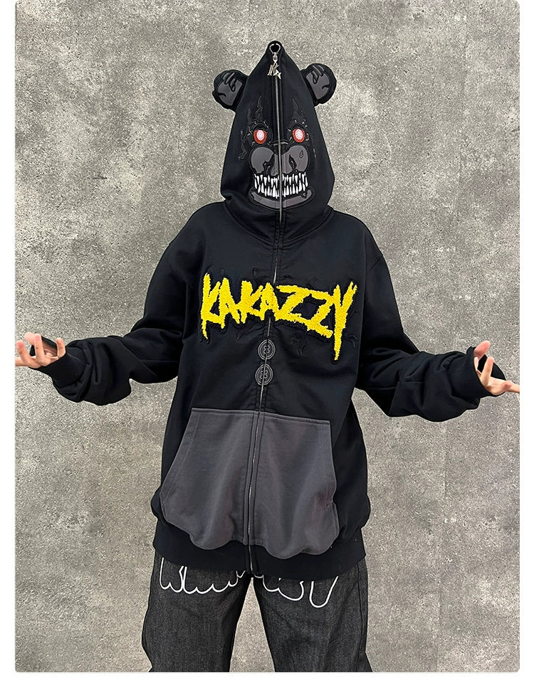 A person is wearing the Seakoff Dark Bear Demon Hoodie, a 400GSM black streetwear piece featuring a graphic bear with red eyes and sharp teeth on the hood. "KAKAZY" in bold yellow letters decorates the chest, ideal for horror fans. The backdrop is a plain gray wall.