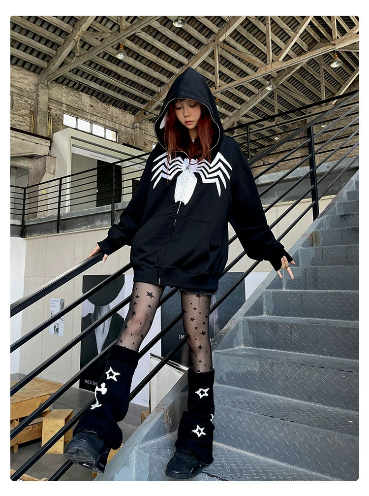 A person in a Seakoff Venom Spider Hoodie—an oversized black and white zip-up sweatshirt—paired with black star-patterned tights and leg warmers, stands on an industrial-style staircase indoors, crafting a striking look sure to captivate streetwear enthusiasts.