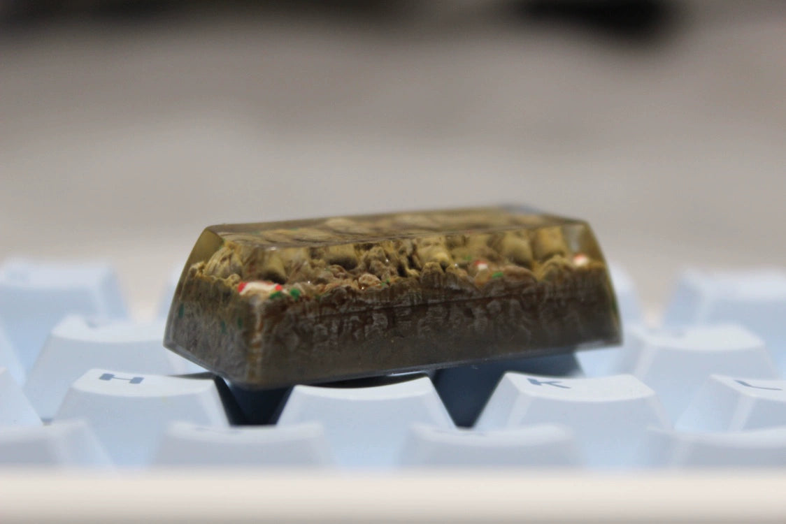 A detailed close-up of the custom "Hokage Monument Keycap – Naruto Hokage Faces" features a miniature landscape with small figures and terrain details on a beige resin backdrop. Compatible with Cherry MX switches, it is showcased on a white keyboard. Brand: Naruto.