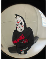 A person sits on a bench wearing a Seakoff Friday the 13th Hoodie, a 400GSM oversized Jason Mask zip-up ideal for horror fans. Their face is hidden by a mask featuring black and red designs. The fisheye lens effect distorts the room&