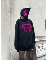 Wearing the Seakoff Futuristic Warrior Hoodie, an oversized 400GSM pink and black zip-up sweatshirt with mask-like patches embodying sci-fi streetwear, a person stands against a white wall. Star-patterned tights complete the look near a labeled "INCU SHOP" machine.