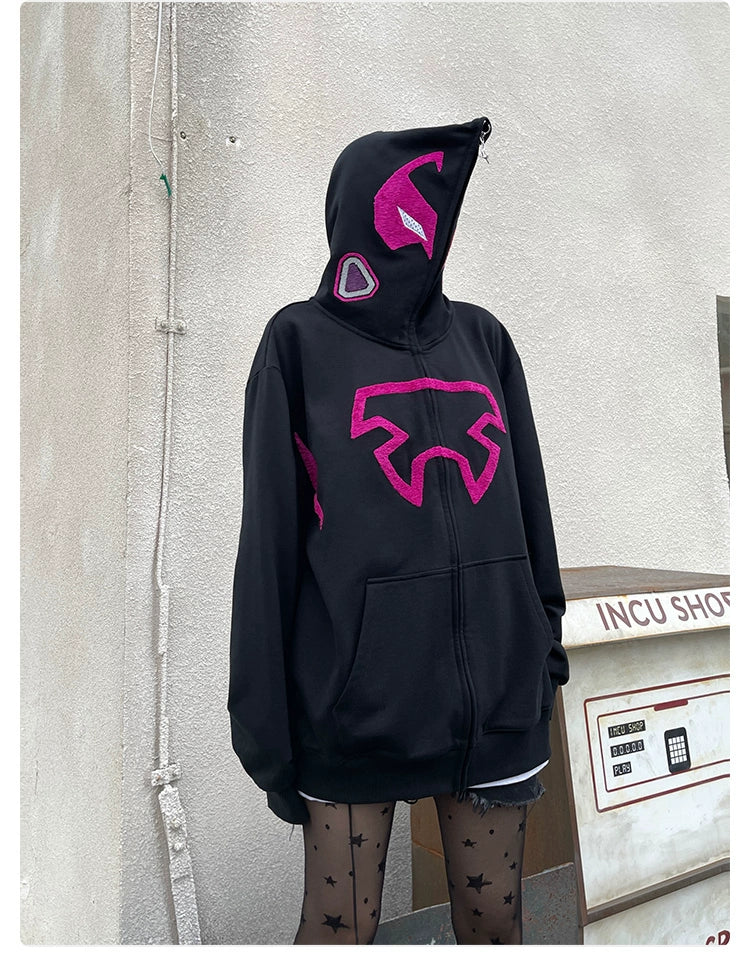 Wearing the Seakoff Futuristic Warrior Hoodie, an oversized 400GSM pink and black zip-up sweatshirt with mask-like patches embodying sci-fi streetwear, a person stands against a white wall. Star-patterned tights complete the look near a labeled "INCU SHOP" machine.