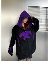 Against a metallic wall, a person wears the Seakoff Dark Hero Hoodie. The black and purple oversized zip-up partially covers their face with its distinctive pattern, evoking a dark hero vibe. Long hair cascades under the hood of this 400GSM streetwear sweatshirt.