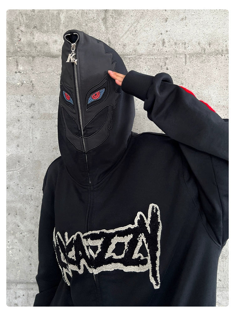 Sporting the Berserk-Inspired Griffith Dark Knight Hoodie, a person zips up the black oversized streetwear hoodie, revealing red eyes and a mask design against a concrete wall. This 400GSM hoodie features bold, stylized white text on the front, embodying Griffith&