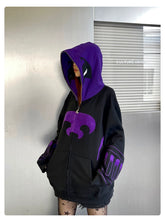 A person wears a Seakoff Dark Hero Hoodie, an oversized 400GSM black and purple superhero zip-up sweatshirt with a large emblem on the front and partial face coverage. They stand before a metallic background under a "CULTURE UNION" sign.