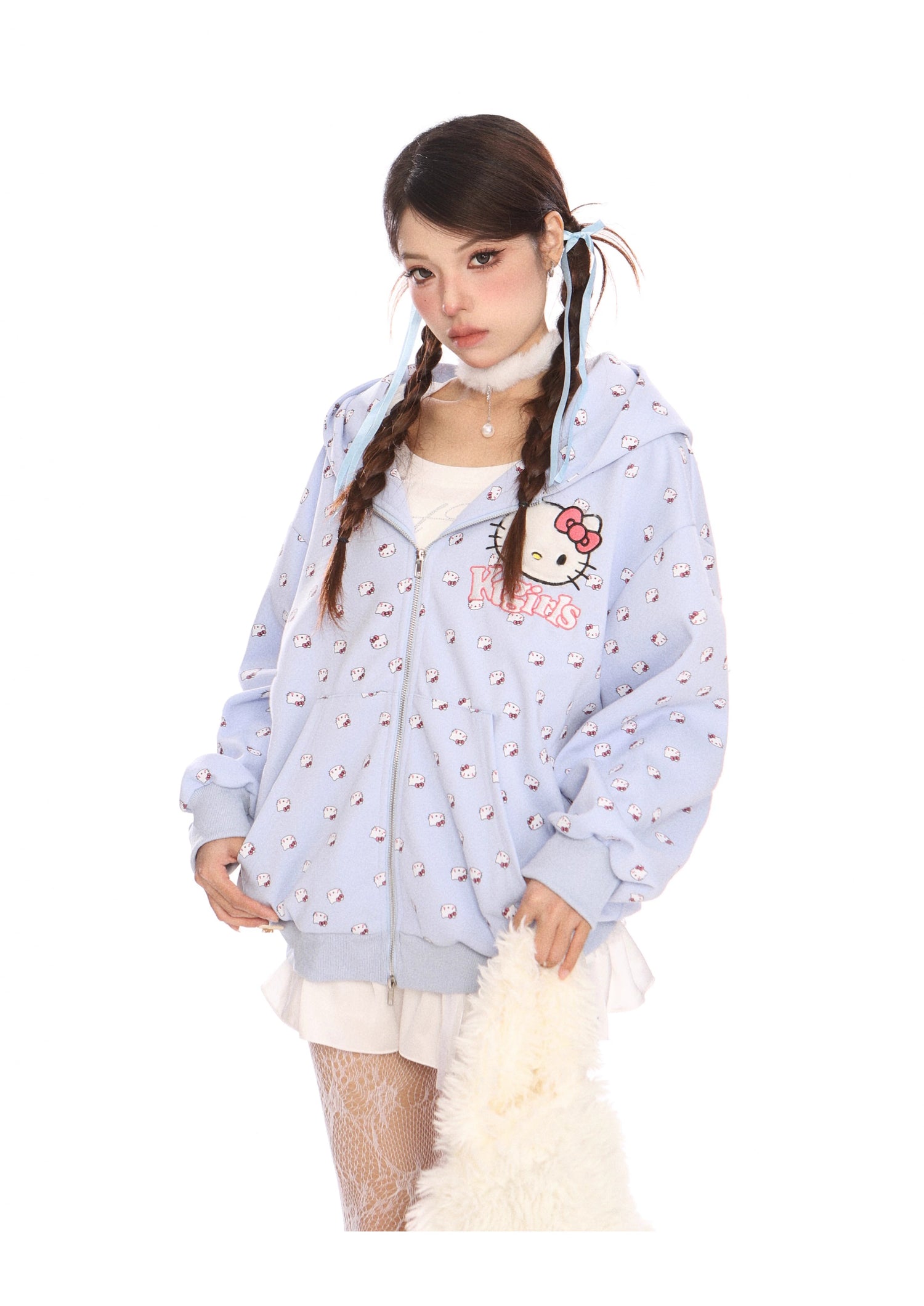 A person sports a Seakoff Hello Kitty Pink Kawaii Hoodie, an oversized zip-up with cat ear hood and all-over print, over a white dress. Their braided hair and fluffy white accessory complete the Kawaii fashion look against a plain white backdrop.