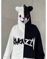A person wears the Seakoff Monokuma-Inspired Hoodie, an oversized black and white zip-up sweatshirt featuring a bear face hood design, ideal for Danganronpa fans. The zip-up front splits into distinct halves with "Kakazy" boldly printed across it.