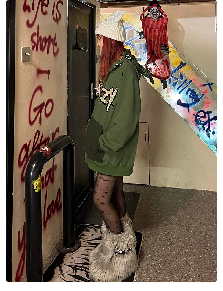 A person in a Seakoff Springtrap-Inspired Hoodie, black patterned tights, furry boots, and a white beanie faces a graffiti-covered wall indoors. With graffiti on the stairs and red-and-black decor above, it&