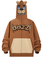 The Seakoff Freddy-Inspired Hoodie is a 400GSM oversized brown hoodie with a zip-up hood creating a bear face, featuring blue eyes and a smiling mouth. It includes beige pockets and stylized Five Nights at Freddy&