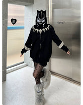 Indoors, someone models an oversized 400GSM Black Panther-inspired hoodie with ear design by Seakoff, paired with star-patterned tights and fuzzy boots. Heart-shaped "love" decor on the wall captures streetwear fans&