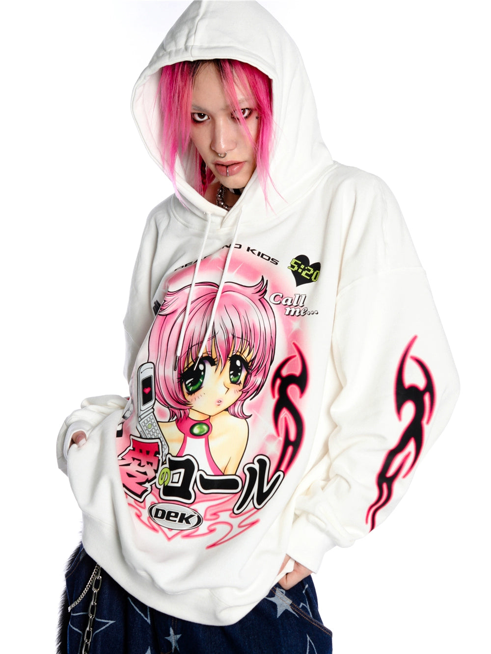 A person with pink hair wears a Seakoff Y2K Aesthetic Anime Hoodie, featuring a retro manga girl graphic holding a kawaii phone. The white hoodie has Japanese text and flame designs on the sleeves. The person looks directly at the camera.