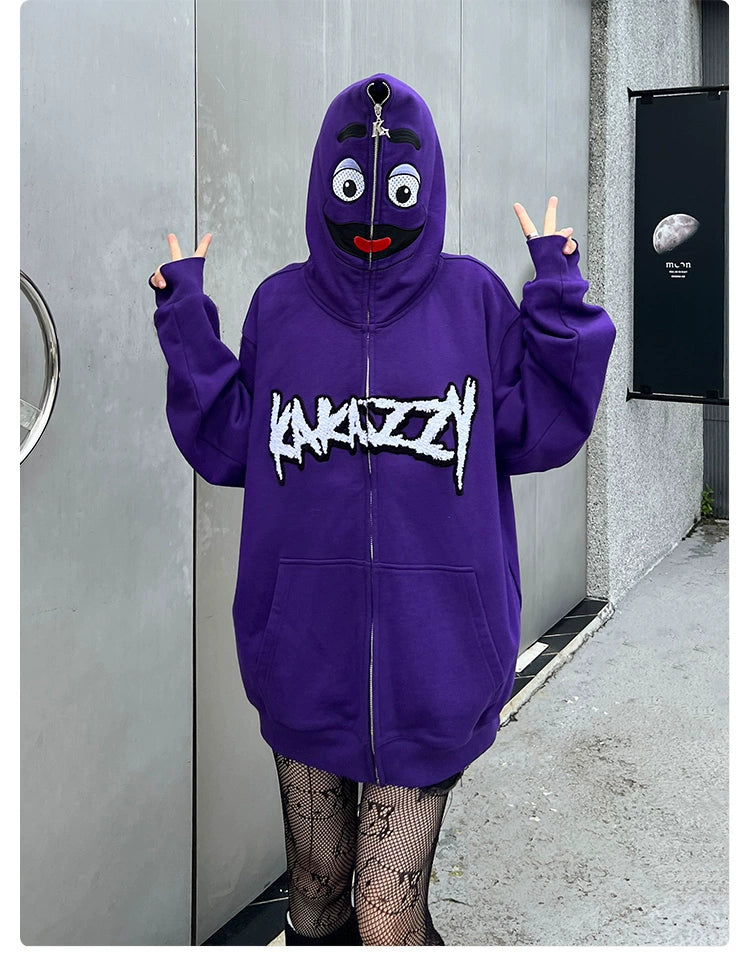 Someone is wearing a Seakoff Fun Cartoon Face Hoodie in bold streetwear style, with "KAYKAZZY" on the front. The oversized purple zip-up features eyes and mouth on the hood, complemented by fishnet stockings as they pose with peace signs.