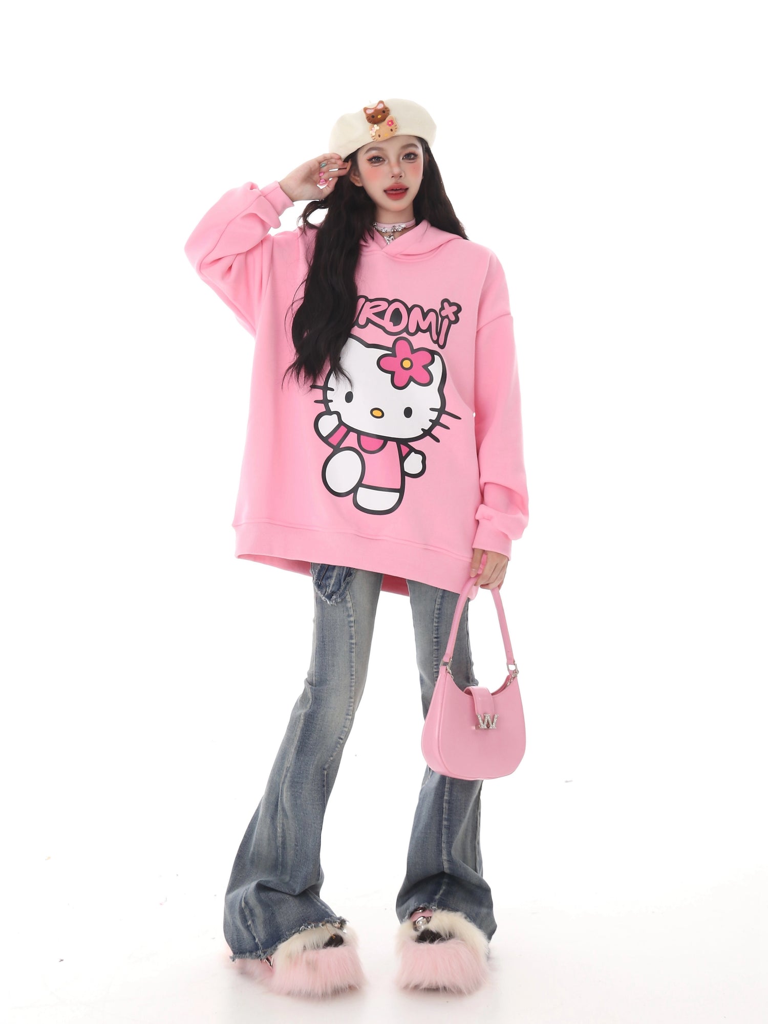Someone dressed in kawaii fashion wears a Seakoff Kawaii Hello Kitty Oversized Hoodie with wide-leg jeans and fluffy pink slippers. They hold a pink handbag and wear a beige beret with a small design, all set against a plain white background, ideal for Sanrio enthusiasts.