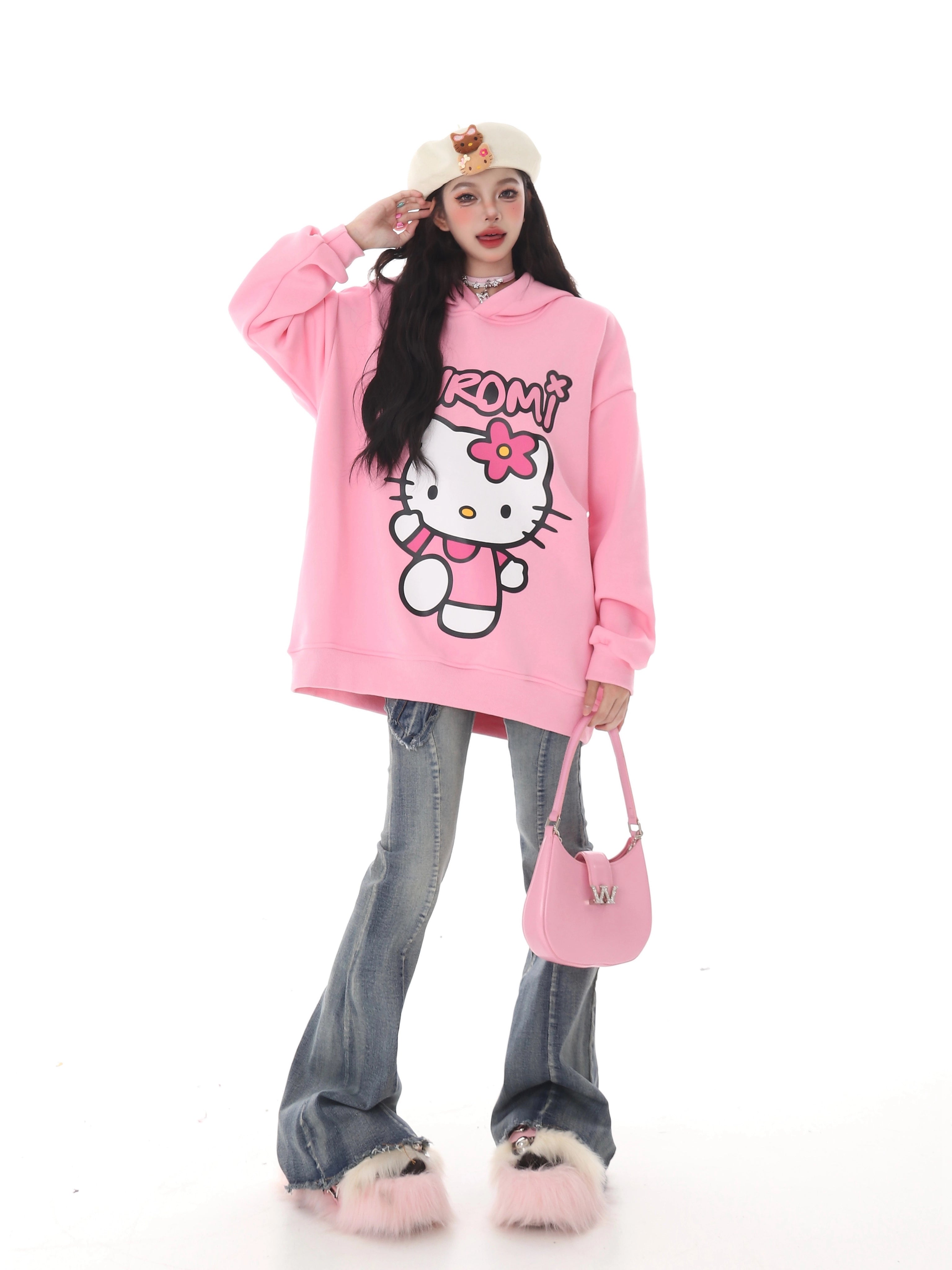 Someone dressed in kawaii fashion wears a Seakoff Kawaii Hello Kitty Oversized Hoodie with wide-leg jeans and fluffy pink slippers. They hold a pink handbag and wear a beige beret with a small design, all set against a plain white background, ideal for Sanrio enthusiasts.