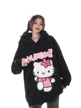 A person wears the Seakoff Kawaii Hello Kitty Oversized Hoodie, featuring a large print of Hello Kitty in a pink outfit. They hold a “Kuromi” sign and sport a pink headband against a white backdrop, embodying kawaii fashion.