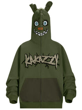 The Seakoff Springtrap-Inspired Hoodie is an oversized green zip-up sweatshirt featuring a cartoon monster face with big eyes and sharp teeth. Perfect for horror game fans, it has "KARAZZI" embroidered in jagged font, evoking Five Nights at Freddy&
