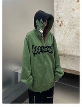 A person wears a Seakoff Hulk-Inspired Hoodie—a green, oversized 400GSM zip-up with an iconic cartoonish angry face on the hood and black chest writing. They stand indoors with distressed walls, making it a perfect pick for streetwear fans.