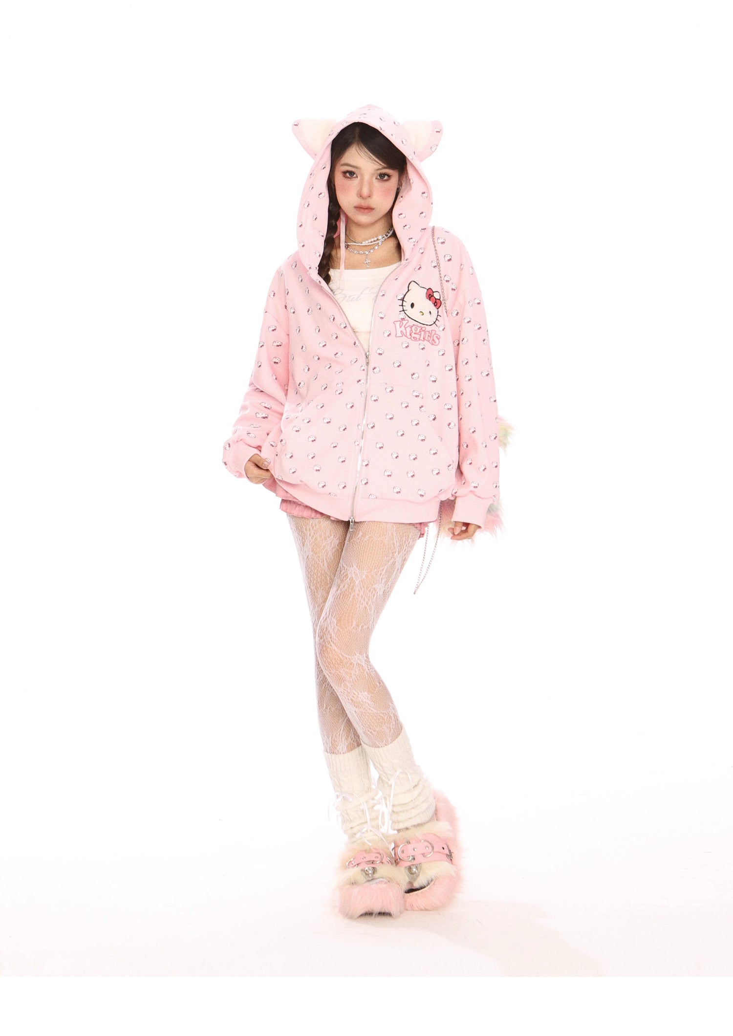 A person poses against a white background in their kawaii fashion, featuring the Seakoff Hello Kitty Pink Kawaii Hoodie—an oversized zip-up with a cat ear hood and all-over print—paired with white lace leggings and fuzzy pink slippers. The ensemble perfectly captures the essence of Sanrio characters.