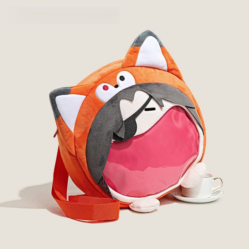 The Seakoff Adorable Fox Plush Shoulder Bag, designed in a cute round orange fox shape with large ears and a transparent mouth pocket, has a red strap and sits beside a small white teacup and saucer.