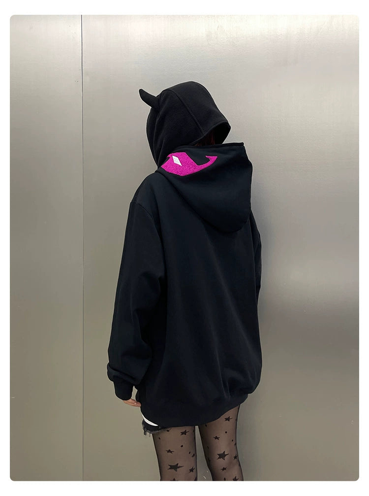 A person wears the Seakoff Futuristic Warrior Hoodie, a black 400GSM oversized sci-fi zip-up sweatshirt featuring cat ears and a pink cat face on the back. Standing against a gray background, they pair it with star-patterned black tights for a bold streetwear statement.