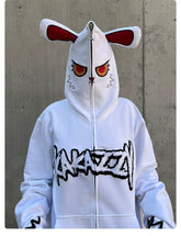 Someone is wearing the Seakoff Fierce Bunny Hoodie - a statement piece with an oversized fit, featuring a red-eyed bunny ear design and embroidered face on the hood. Bold black text adorns the front against a simplistic gray concrete wall, enhancing its striking appearance.