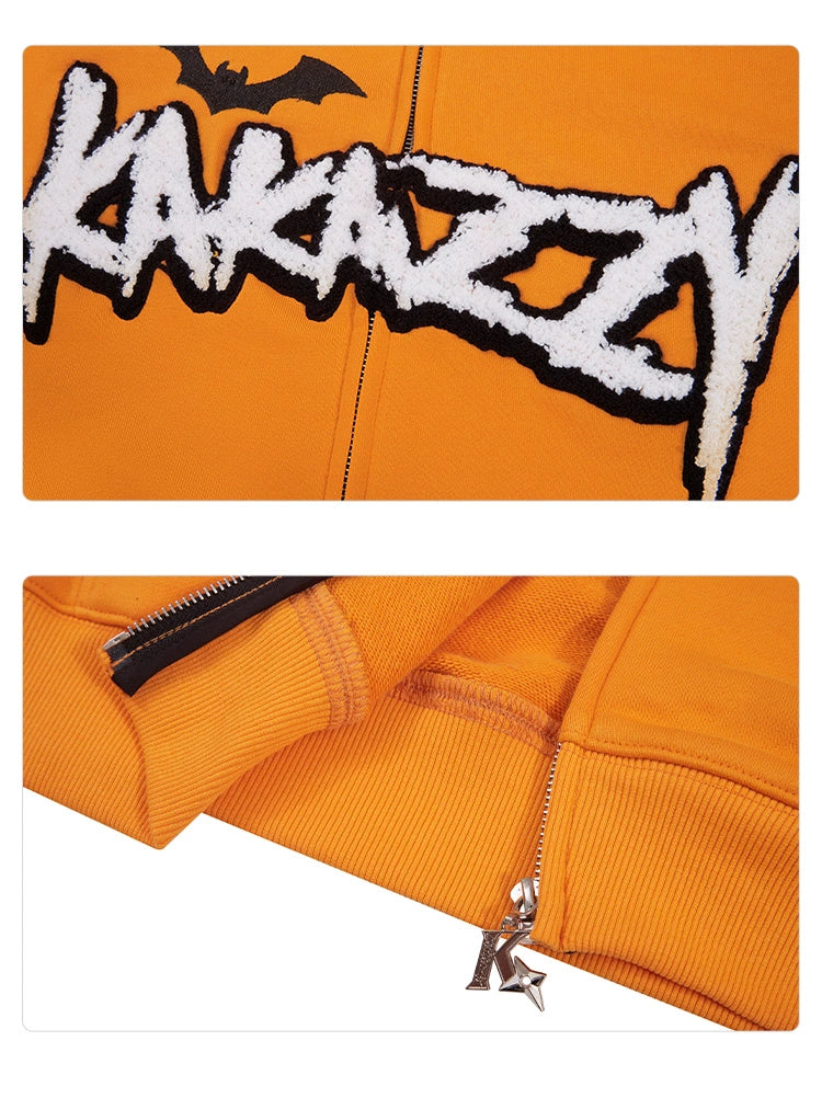 A close-up of the Seakoff Halloween Pumpkin Hoodie, a 400GSM oversized orange zip-up sweatshirt. It features bold "KAKAZZY" text with a bat symbol above and a detailed zipper with a jack-o&