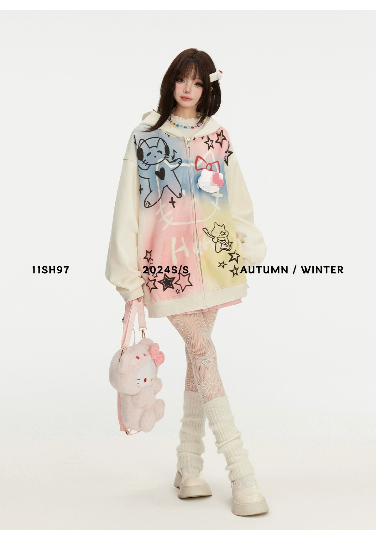 A model showcases the Seakoff Pastel Cat Graffiti Hoodie featuring colorful cat and star graphics for a streetwear vibe. She carries a matching kawaii plush bag, with knee-high socks and chunky shoes completing the look. Text reads "11SH97" and "2024 S/S AUTUMN / WINTER.