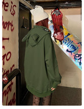 A person with long hair, wearing a white beanie and a Seakoff Springtrap-Inspired Hoodie—400GSM Oversized Green Zip-Up from the Five Nights at Freddy&