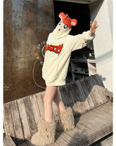 Wearing Seakoff’s Cute Hamster Cartoon Hoodie, featuring playful ears and fluffy boots, a person stands on a wooden bench with outstretched arms in front of a metal panel and bustling shelf—a perfect scene for cartoon lovers!.