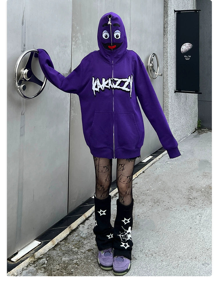 A person in a Seakoff Fun Cartoon Face Hoodie, an oversized purple zip-up streetwear sweatshirt, leans against a metallic wall. They wear fishnet tights, black leg warmers with white stars, and purple shoes. A black poster is partially visible on the wall.