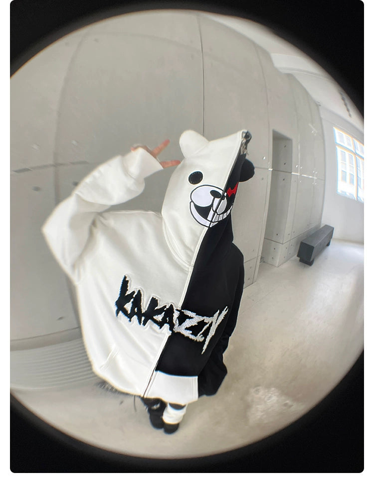 A person dons a Seakoff Monokuma-Inspired Hoodie, an oversized 400GSM black and white zip-up with a bear face on the hood. "Kavazy" is printed on the back. Ideal for Danganronpa fans, this fisheye lens image captures them in a minimalist room.
