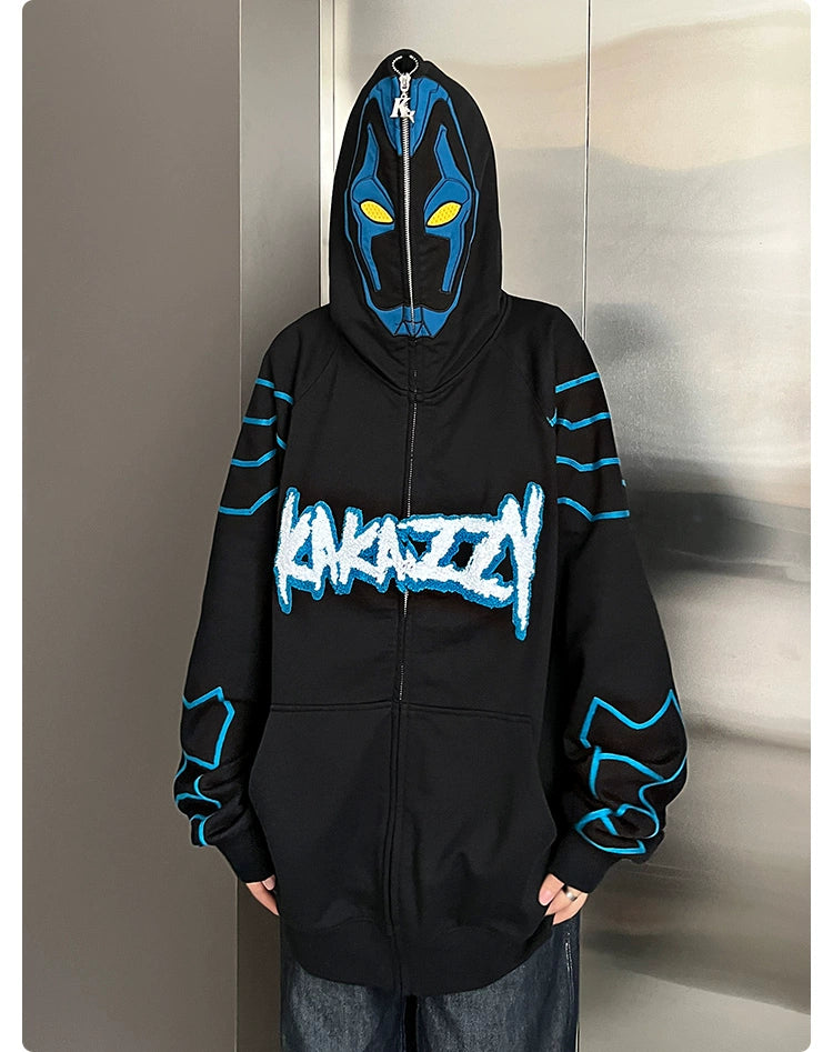 A person in a Seakoff Cyberpunk Superhero-Inspired Hoodie, an oversized black zip-up sci-fi sweatshirt, stands against a metallic wall. The 400GSM hoodie features a mask design on the hood and "Kakazzy" graphic on the front, ideal for fans of futuristic styles.