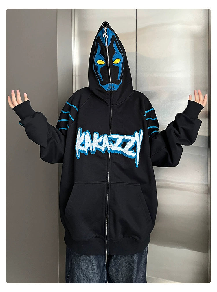 Wearing a Seakoff Cyberpunk Superhero-Inspired Hoodie, a black 400GSM oversized sci-fi sweatshirt with blue and white graffiti text, the person exudes futuristic style. The hood reveals a striking mask with yellow eyes as they stand poised for adventure.
