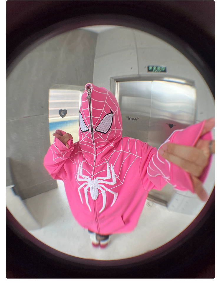 A person wearing a Seakoff Spider-Inspired Hoodie, a 400GSM oversized pink zip-up superhero sweatshirt, covers their face. Stretching one arm towards the camera creates a dramatic fisheye effect against the gray wall and elevator door—perfect for superhero fans.