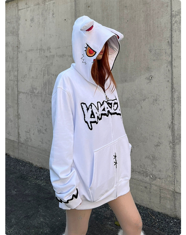 A person with long hair wears a Seakoff Fierce Bunny Hoodie, featuring a stylized face design with red eyes and playful bunny ears. The oversized hoodie stands out against a plain concrete wall.