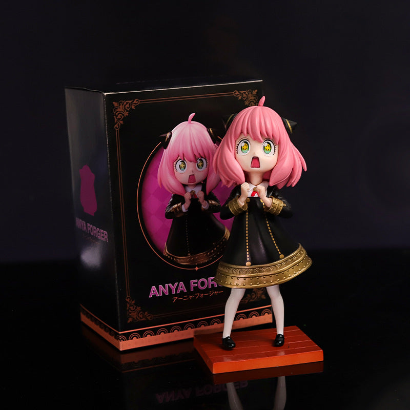 The Spy x Family Anya Forger PVC Figure, featuring a 17 cm pink-haired character with starry eyes, dons a black dress with gold trim and stands on a wooden base. The box showcases artwork of Anya, proudly labeled from "Spy × Family.