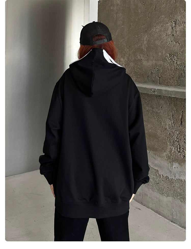 A person with long hair, wearing a Seakoff Scream-Inspired Hoodie—an oversized black zip-up horror movie sweatshirt—faces a concrete wall. Their back is turned towards the camera in a minimalist indoor setting—perfect for horror fans envisioning lurking shadows.