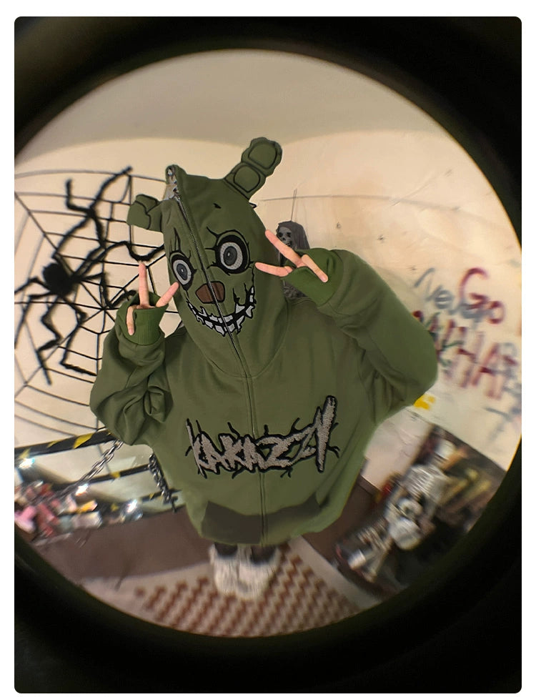 Dressed in a Seakoff Springtrap-Inspired Hoodie, an oversized 400GSM green zip-up sweatshirt with a cartoonish face, the person indoors flashes peace signs. The room, ideal for Five Nights at Freddy&