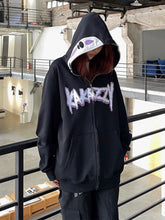 A person indoors wears a black No-Face Anime Hoodie by Spirited Away. The oversized zip-up has "KARAZY" in purple and white with an anime-inspired design. With the hood up, it partially obscures the face, set in a modern industrial space perfect for Spirited Away fans.