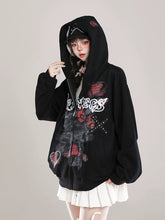 A person in a black Seakoff Gothic Hello Kitty Princess Hoodie, featuring edgy heart and cross graphics, stands against a neutral backdrop. The hoodie artfully blends kawaii fashion with an edge. They pair it with a white skirt, their head tilted and hand on the hood.