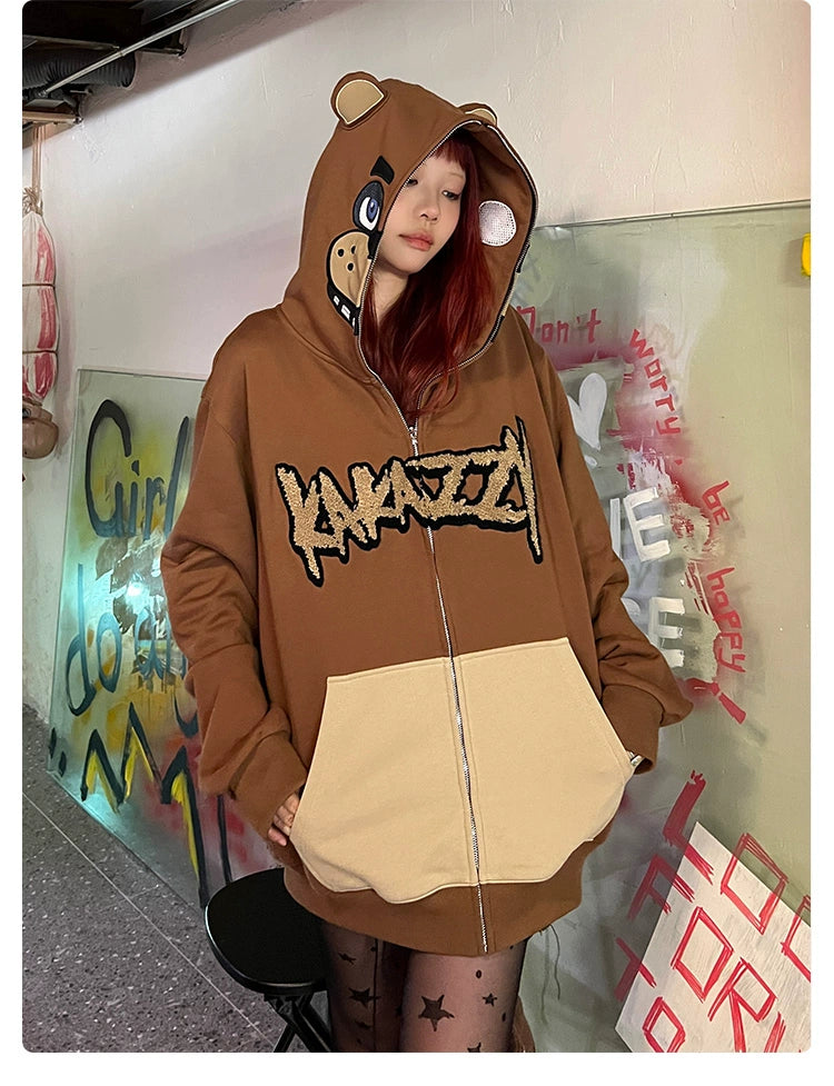 In front of a graffiti wall, a person with long hair wears the Freddy-Inspired Hoodie by Seakoff, an oversized brown zip-up Five Nights at Freddy&