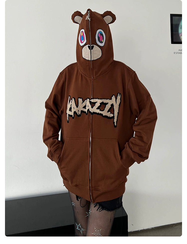 A person wears a Seakoff Cute Bear Hoodie—a 400GSM oversized brown zip-up with ears—and pairs it with sheer, star-patterned tights, creating a bold streetwear look against a plain white wall.