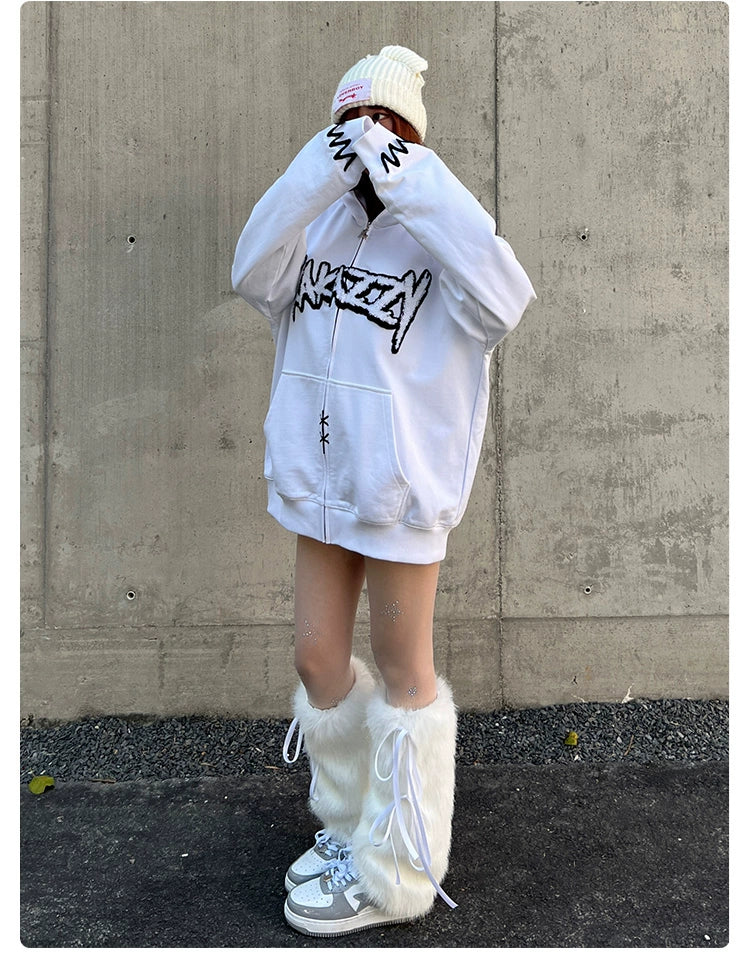 A person stands against a concrete wall, wearing the oversized Seakoff Fierce Bunny Hoodie with graffiti-style text and rabbit ear design. They cover their face with the sleeves, paired with fluffy white leg warmers over sneakers for a look that&