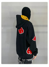 A person in a Seakoff Uchiha Obito-Inspired Hoodie, featuring the Akatsuki cloud design with spiral mask, stands facing a gray wall. They&