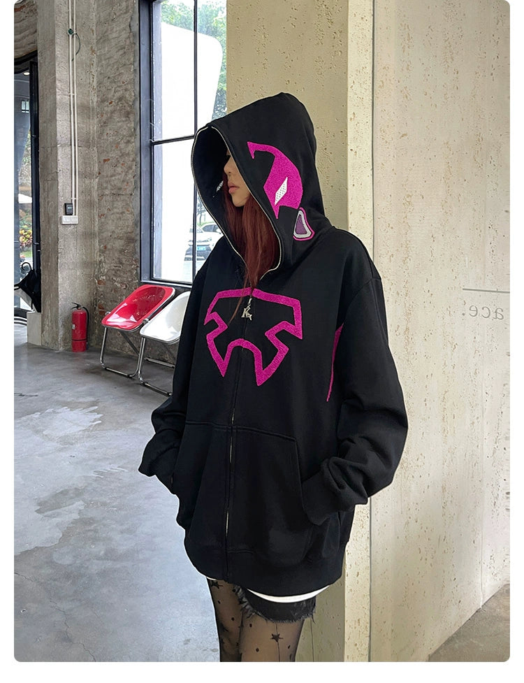 Standing in a room with concrete walls and large windows, a person wears the Seakoff Futuristic Warrior Hoodie, an oversized 400GSM pink and black zip-up sweatshirt. With hands tucked in pockets, long hair, and patterned tights, they exude a sci-fi streetwear vibe.